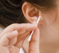 Woman is cleaning ear with a cotton swab