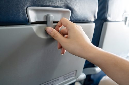Hand of asian female passenger try to open a tray in front of the seat in low cost airplane by slide to unlock and ready for inflight meal or food service. Plastic table in back seat in economy class.