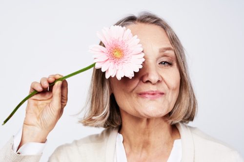 Cheerful elegant elderly woman holding a flower near her face