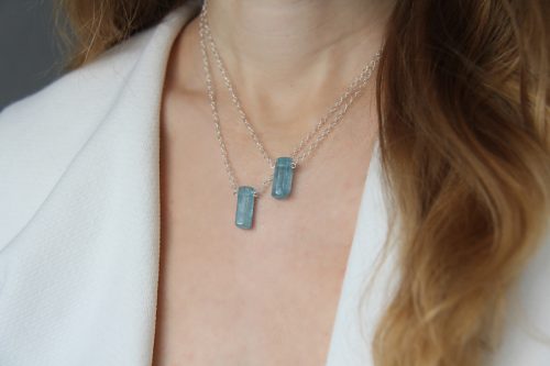 View of an aquamarine necklace on a woman with long hair and a white shirt.