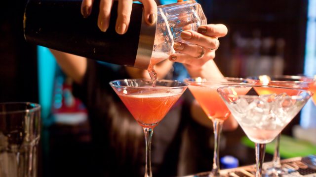 Close up of a female bartender pouring pink cocktails into martini glasses.