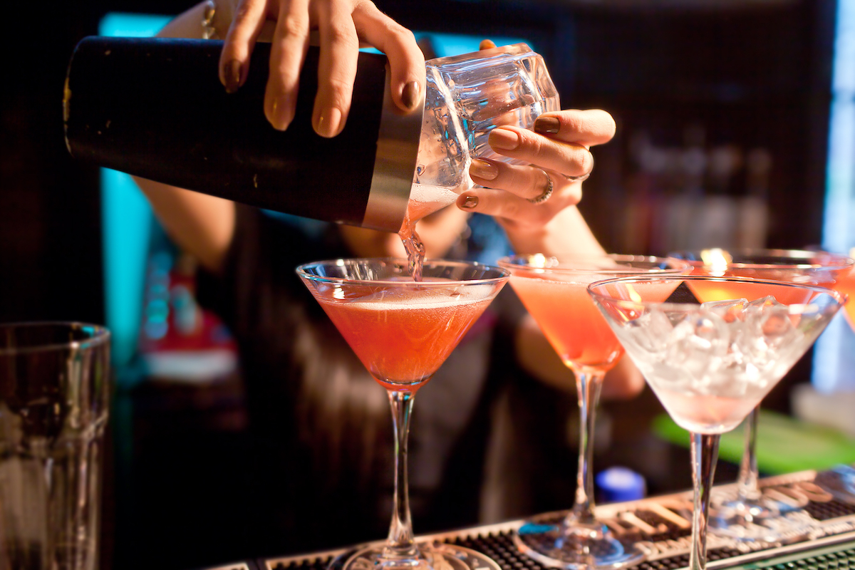 Close up of a female bartender pouring pink cocktails into martini glasses.