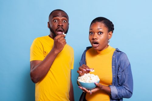 couple eating popcorn and looking shocked