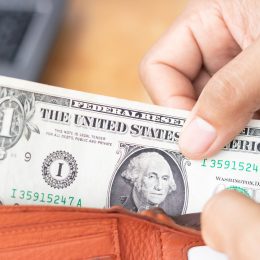 A hand pulling a one dollar bill out of a wallet