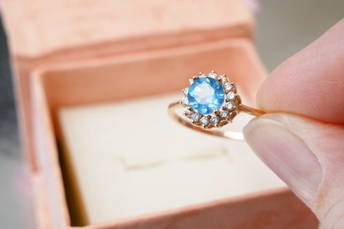 Hand pulling a blue topaz and diamond ring out of a box
