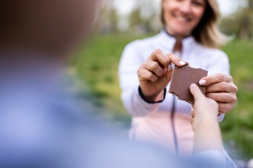 An unrecognizable girl shares chocolate with her mother outdoors