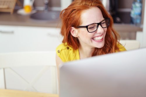 redheaded woman laughing at the list of funny wifi names on her laptop