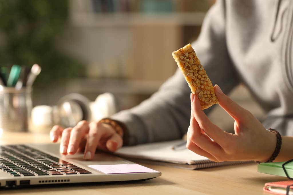 Closeup of a hand holding a granola bar while using a laptop