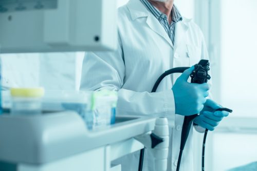 Cropped photo of a doctor in white coat and rubber gloves standing with a modern endoscope