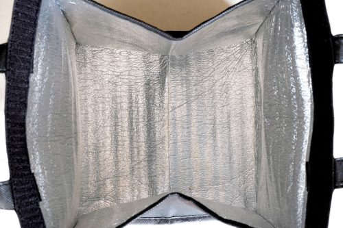 Inside of an opened foldable insulated thermal bag, showing the padded silver aluminum foil or insulating material to keep meals warm or cold, conveniently use for delivery or transporting food.