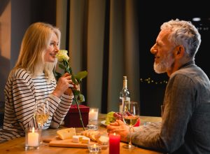 A happy couple in their 50s enjoying a dinner date; the woman is smelling a rose