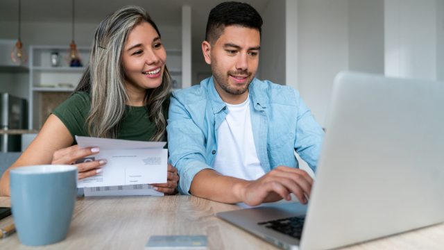A smiling couple sitting at a table filing their taxes on a laptop