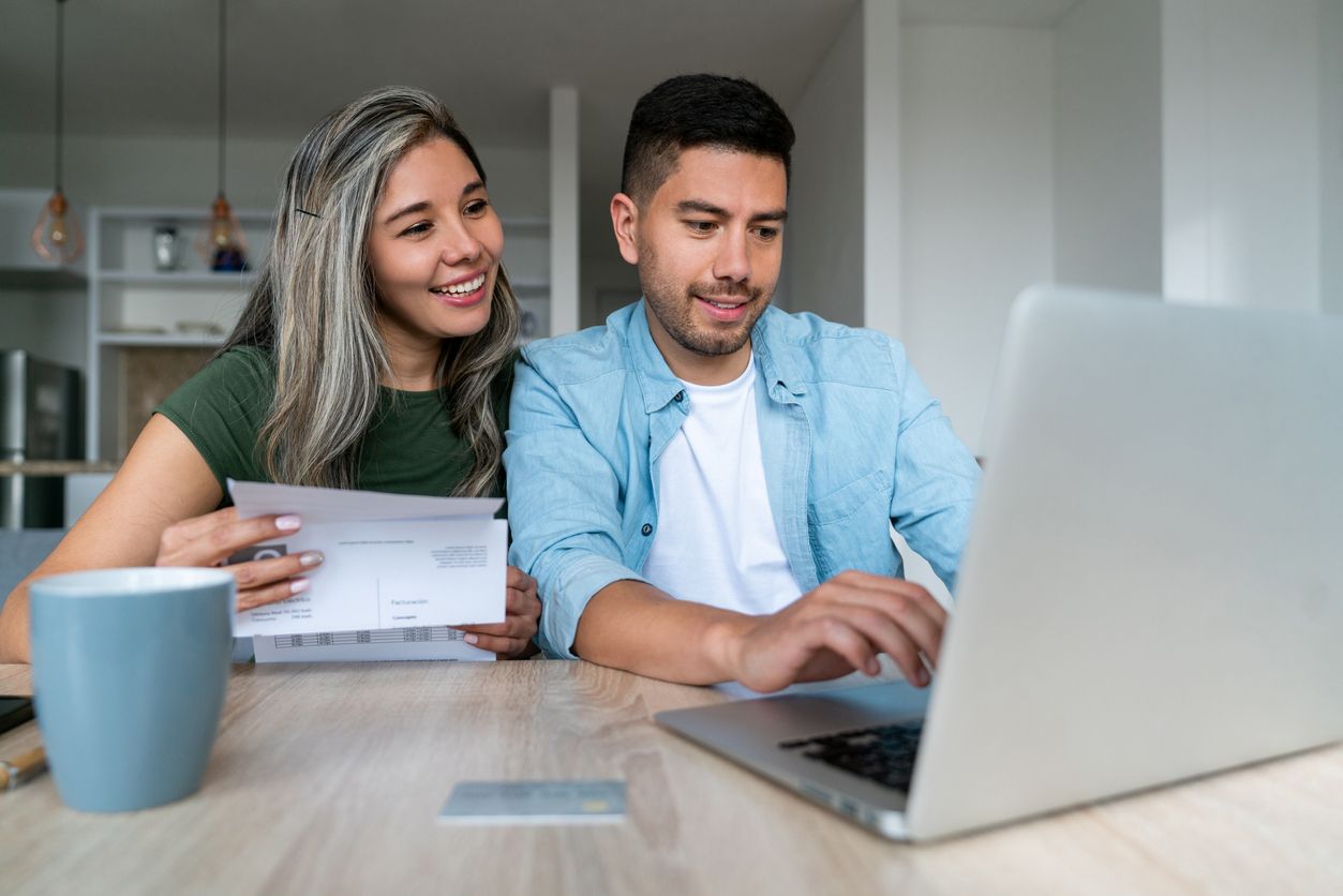 A smiling couple sitting at a table filing their taxes on a laptop