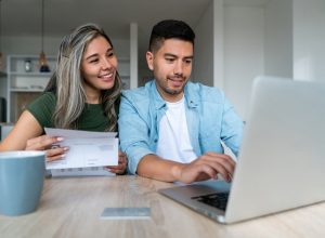 A smiling couple sitting at a table filing their taxes on a laptop