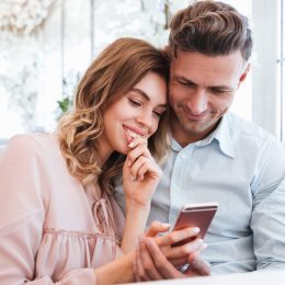 Family portrait of happy couple man and woman resting in restaurant and watching on mobile phone together on date