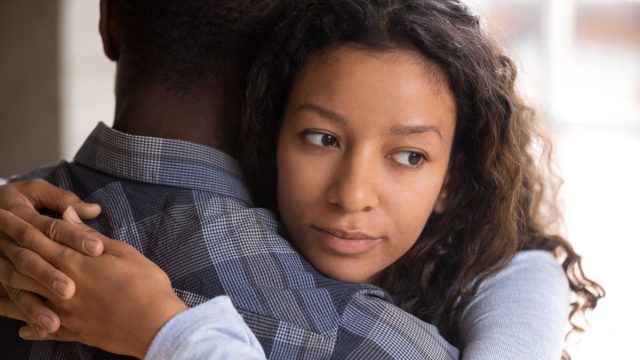 young black couple hugging, but woman looks doubtful