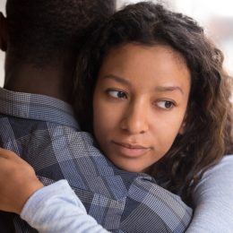 young black couple hugging, but woman looks doubtful