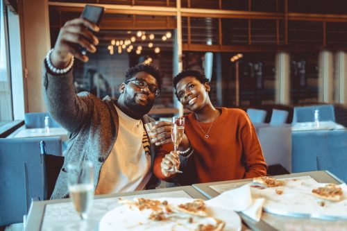 Friends gathered at the restaurant eating pizza and drinking some wine and spirit. At this photo they capturing a selfie photo while making a toast.