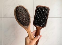 Female Hand Holding an Old Being Used Wooden Hairbrush and a New Wooden Hairbrush Horisontal