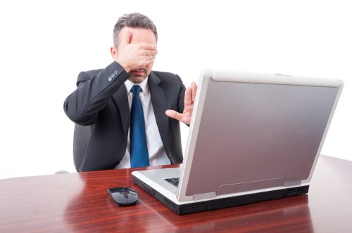 man covering his eyes in front of his computer—a victim of april fools pranks