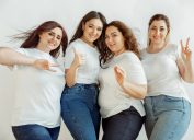 Bốn bạn nữ tạo dáng chụp ảnh và giơ dấu hòa bình, tất cả đều mặc áo phông trắng và quần jean