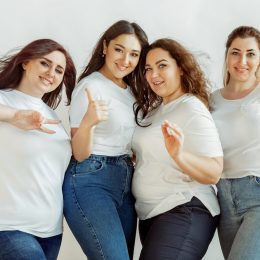 Four female friends posing and giving the peace sign, all wearing white t-shirts and jeans