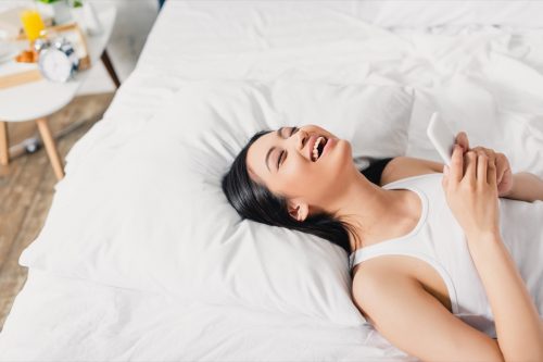 woman laying on her bed laughing at 'good morning text messages' for her