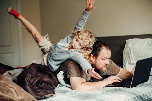 overwhelmed father looking up funny quotes on his laptop while his young daughter climbs on his back