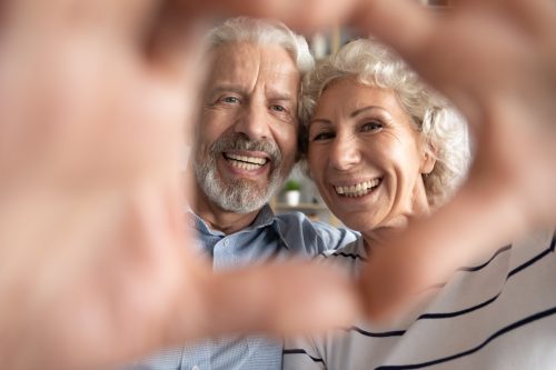 older couple making a heart sign with their hands smiling at the camera