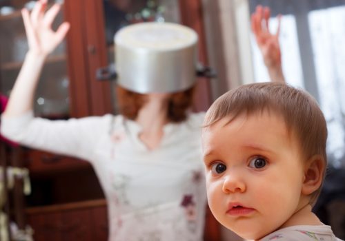baby looks frightened as mother puts pot over her head