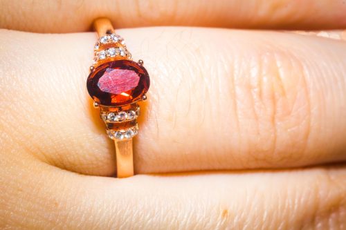 Close up of a hand with a garnet ring that has diamonds on the side and a gold band