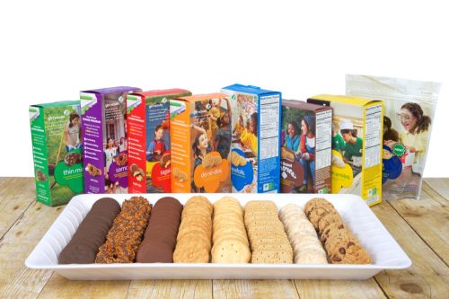 White tray with 8 varieties of Girl Scout Cookies on a wood table, boxes standing behind plate. Available annually during Girl Scout cookie sales from ABC Bakers