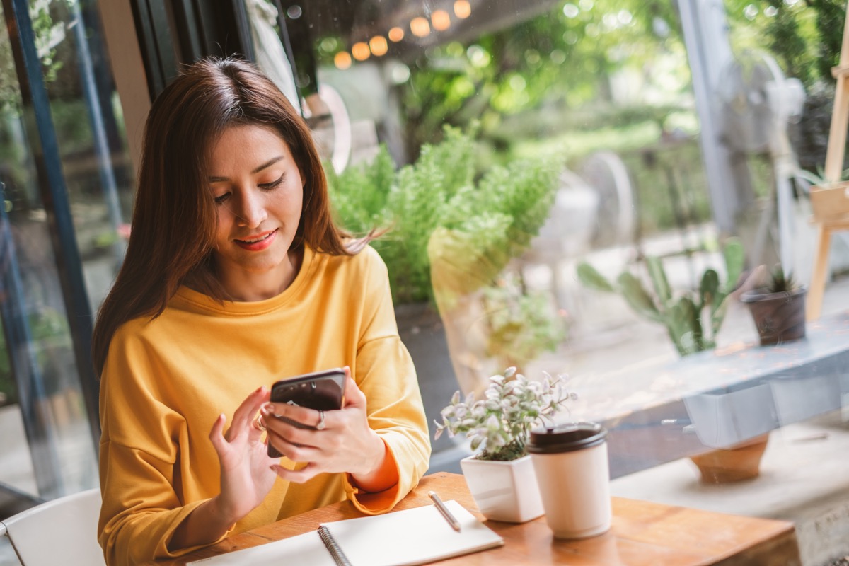 woman at a cafe responding to good morning messages for her on her phone