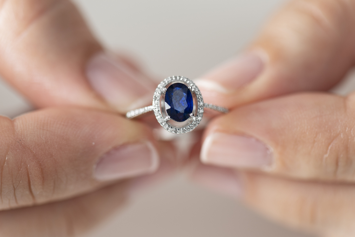 Close up of hands holding a sapphire and diamond ring