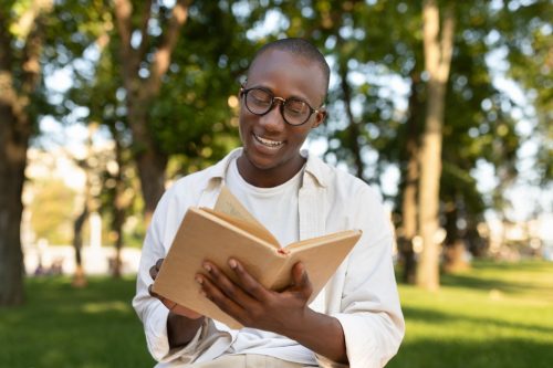 young black man smiling and reading a book outside