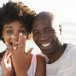 Cropped photo of a happy young couple taking a selfie on the beach, showing off their engagement ring.