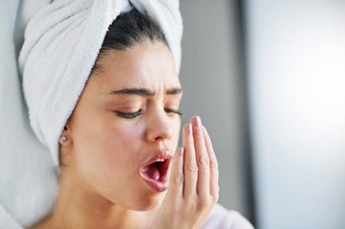 Woman with a towel wrapped around her head, checking her breath.