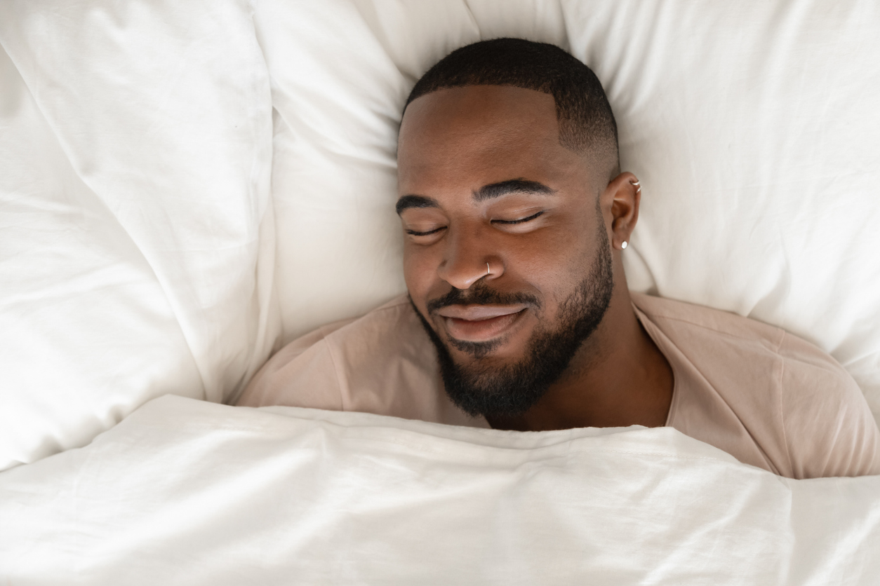 Nhìn từ trên xuống người đàn ông Mỹ gốc Phi hạnh phúc đang ngủ trên chiếc giường trắng thoải mái nhìn thấy giấc mơ đẹp, người đàn ông hai chủng tộc điềm tĩnh cảm thấy mệt mỏi đang ngủ trong phòng ngủ thoải mái dưới tấm ga trải giường