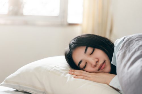 Young adult asian woman sleep in bedroom on morning. Stay at home tired from study and work resting on bed and pillow.