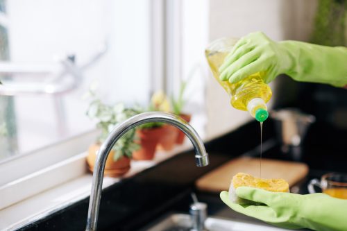 Person using dish soap over a kitchen sink.