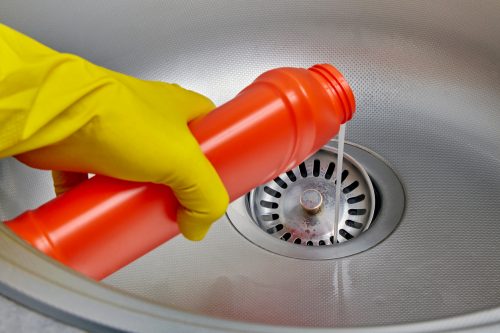Hand pouring drain cleaner into a sink drain.