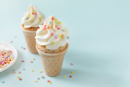 Mini party cakes in wafer ice cream cones topped with butter cream soft cheese frosting and colorful chocolate sprinkles, fun dessert