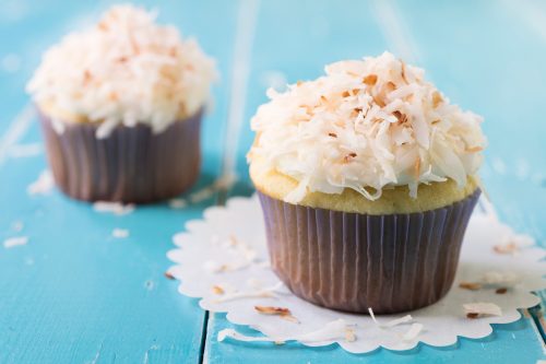 Two almond cupcakes with toasted coconut topping on a blue table.
