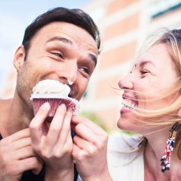 Joyful couple eating cupcake outdoors