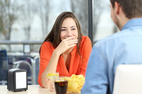 Woman at a restaurant covering her mouth to hide her teeth.