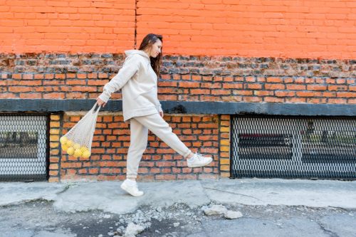Adult woman in beige suit walks down street carrying eco friendly cotton bag filled with lemons