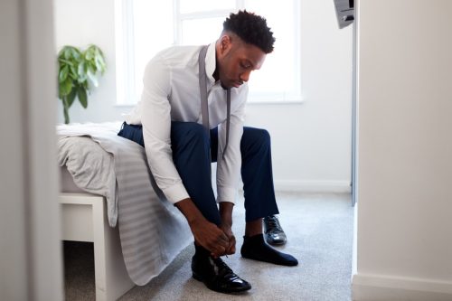 man sitting on his bed putting his shoes on while getting ready for work