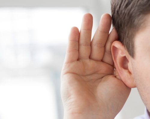 man holding his hand near his ear listening closely