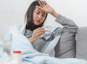 young asian woman taking her temperature and feeling sick