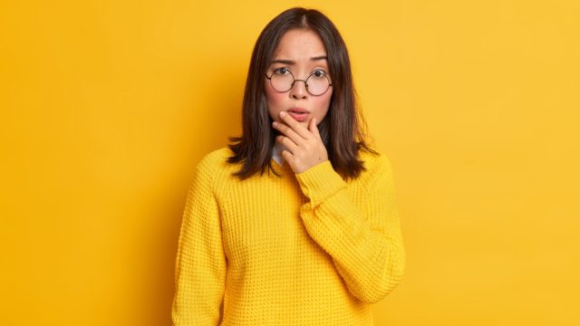 woman in glasses holding her chin looking confused